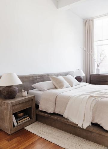 Minimalist organic modern bedroom with reclaimed wood headboard, crisp white linens, natural fiber rug, and soft sculptural bedside elements
