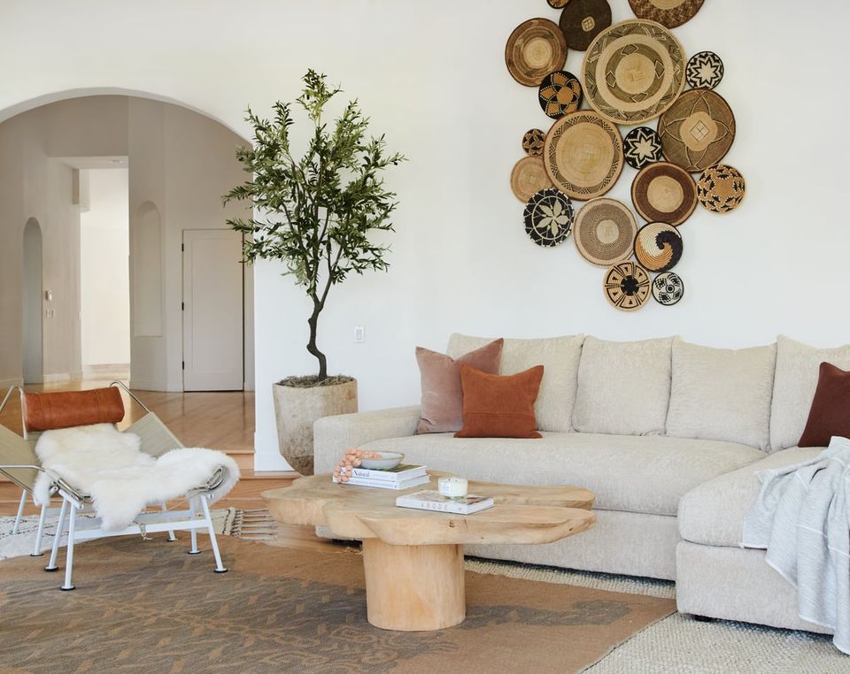 Scandinavian living room with warm neutrals, woven basket wall art, cream sectional, rust accents, and natural wood coffee table