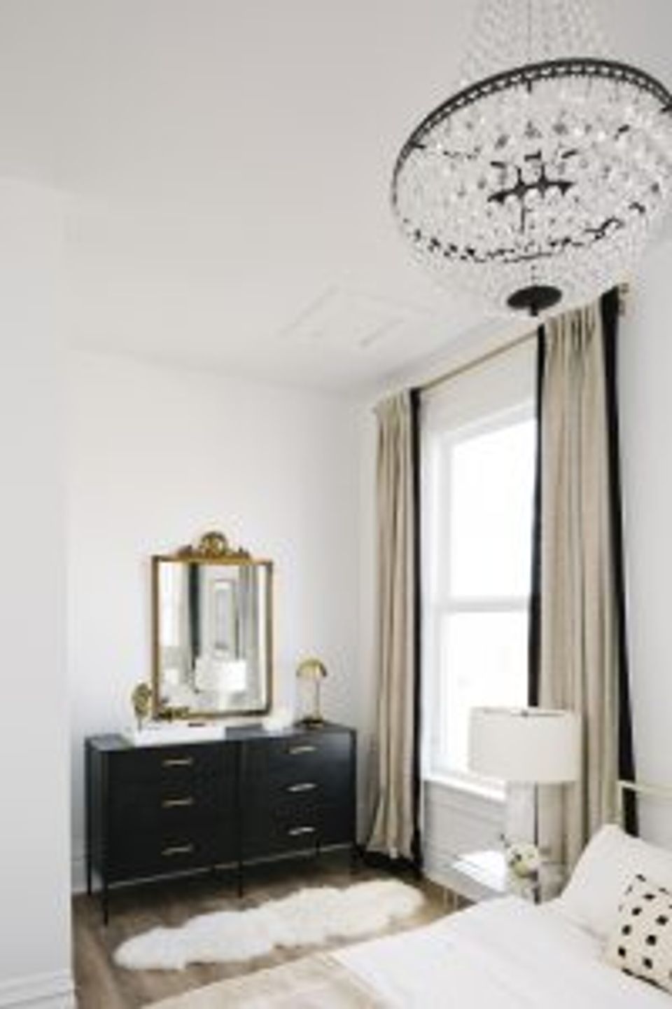 Elegant bedroom with black dresser, cream drapes, crystal chandelier, and classic-modern aesthetic