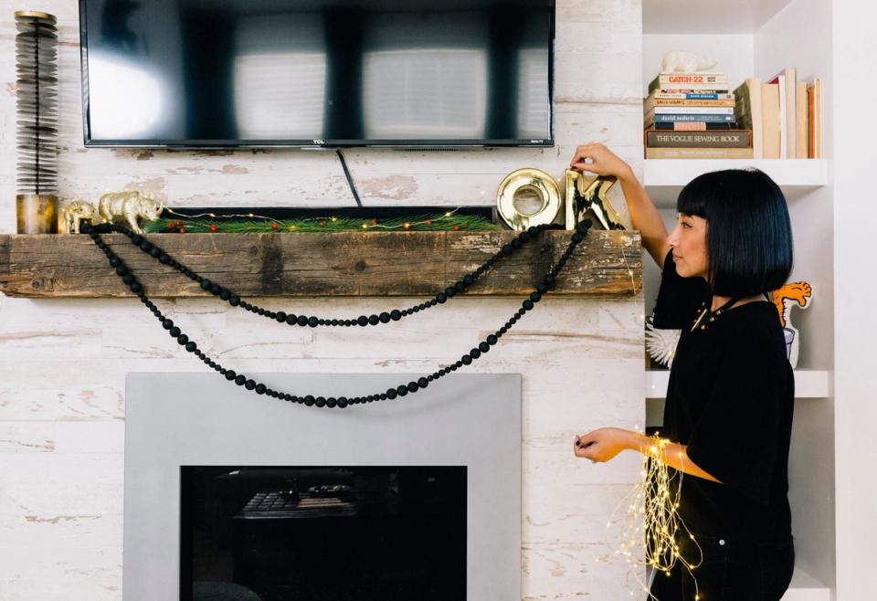 Modern fireplace mantel with black garland swag, brass accents, and styled shelving in minimalist aesthetic