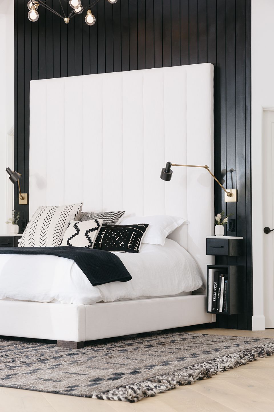 Contemporary monochrome bedroom: black shiplap walls, white tall headboard, industrial lighting, minimal