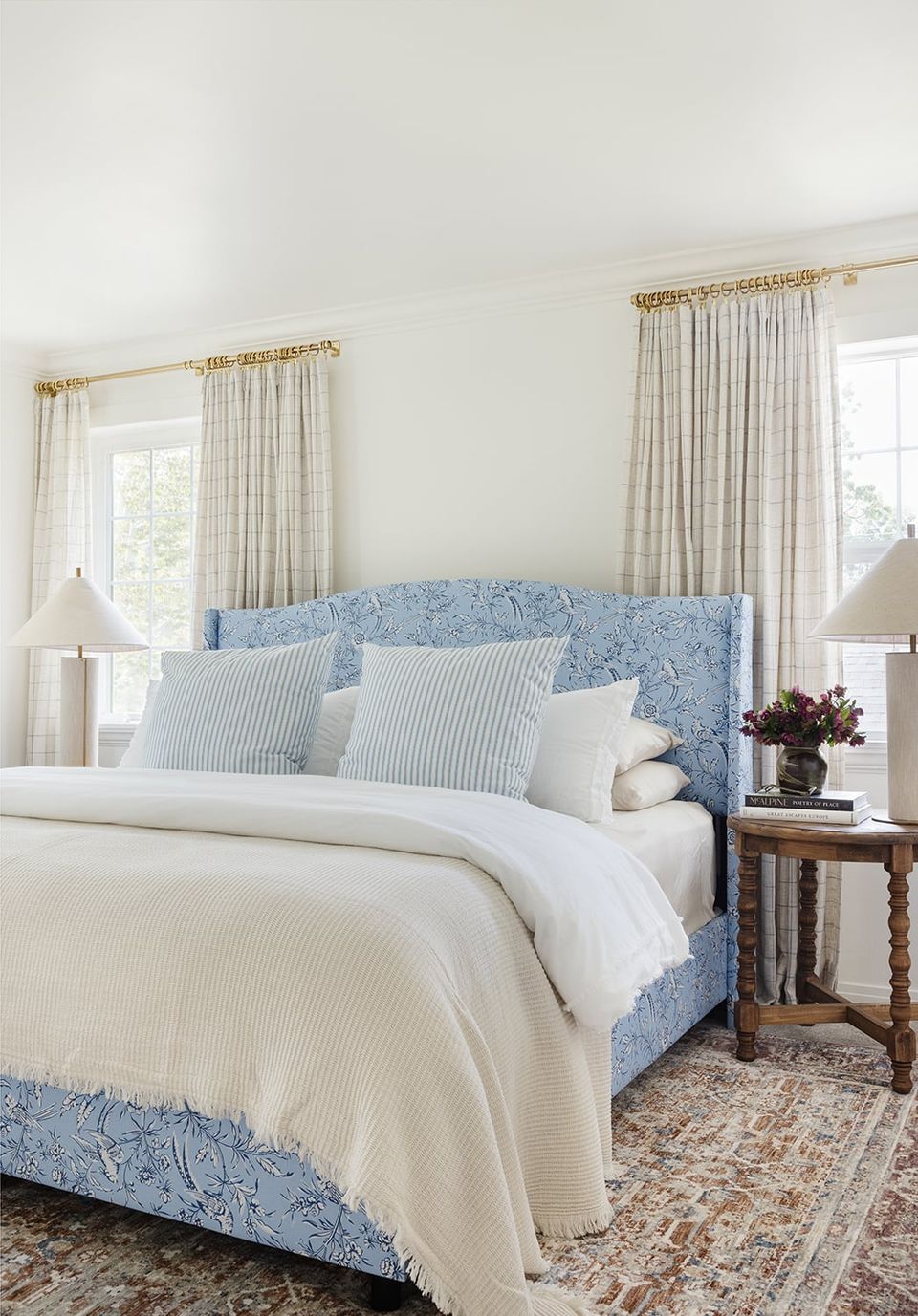 Serene coastal bedroom with blue patterned headboard, crisp white linens, and layered striped pillows in soft blue and cream tones