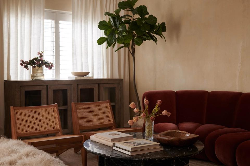 Warm contemporary living room blending deep burgundy velvet seating with wood furnishings and natural greenery in soft, inviting tones