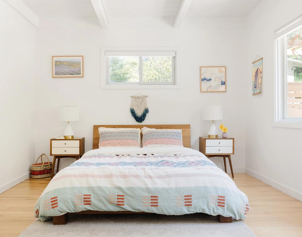 Bright mid-century bedroom with light wood nightstands, geometric patterned duvet, hardwood floors, and minimal decor.