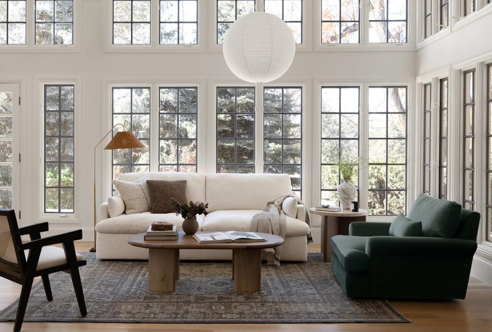 Bright minimalist living room with floor-to-ceiling windows, cream sofa, dark green chair, and natural wood accents
