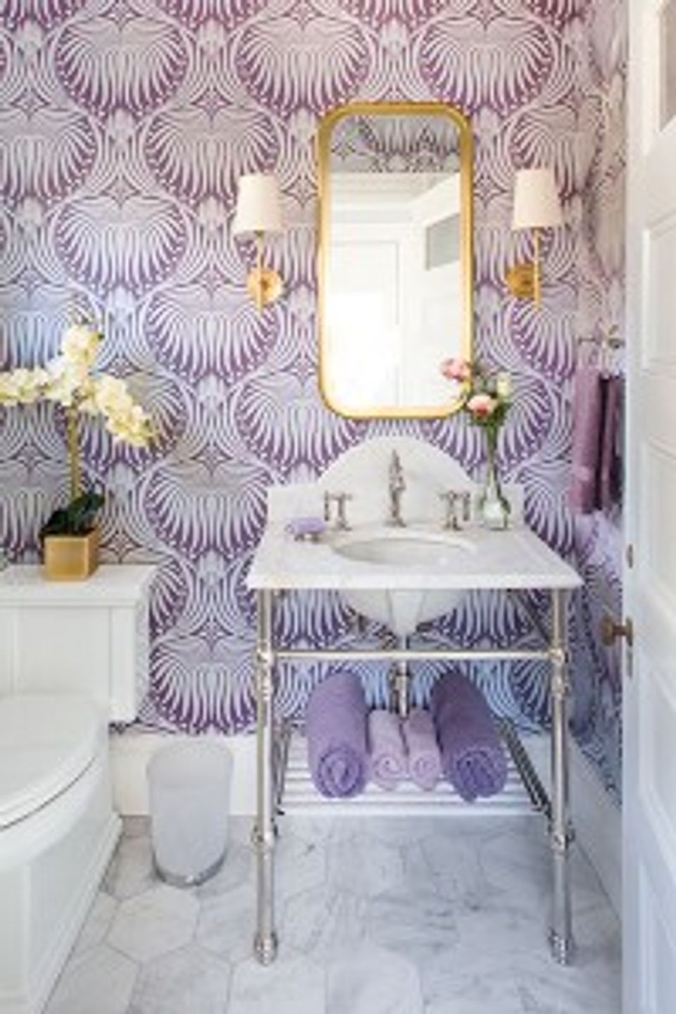 Glamorous lavender bathroom with geometric shell wallpaper, gold-framed mirror, and contemporary vanity styling