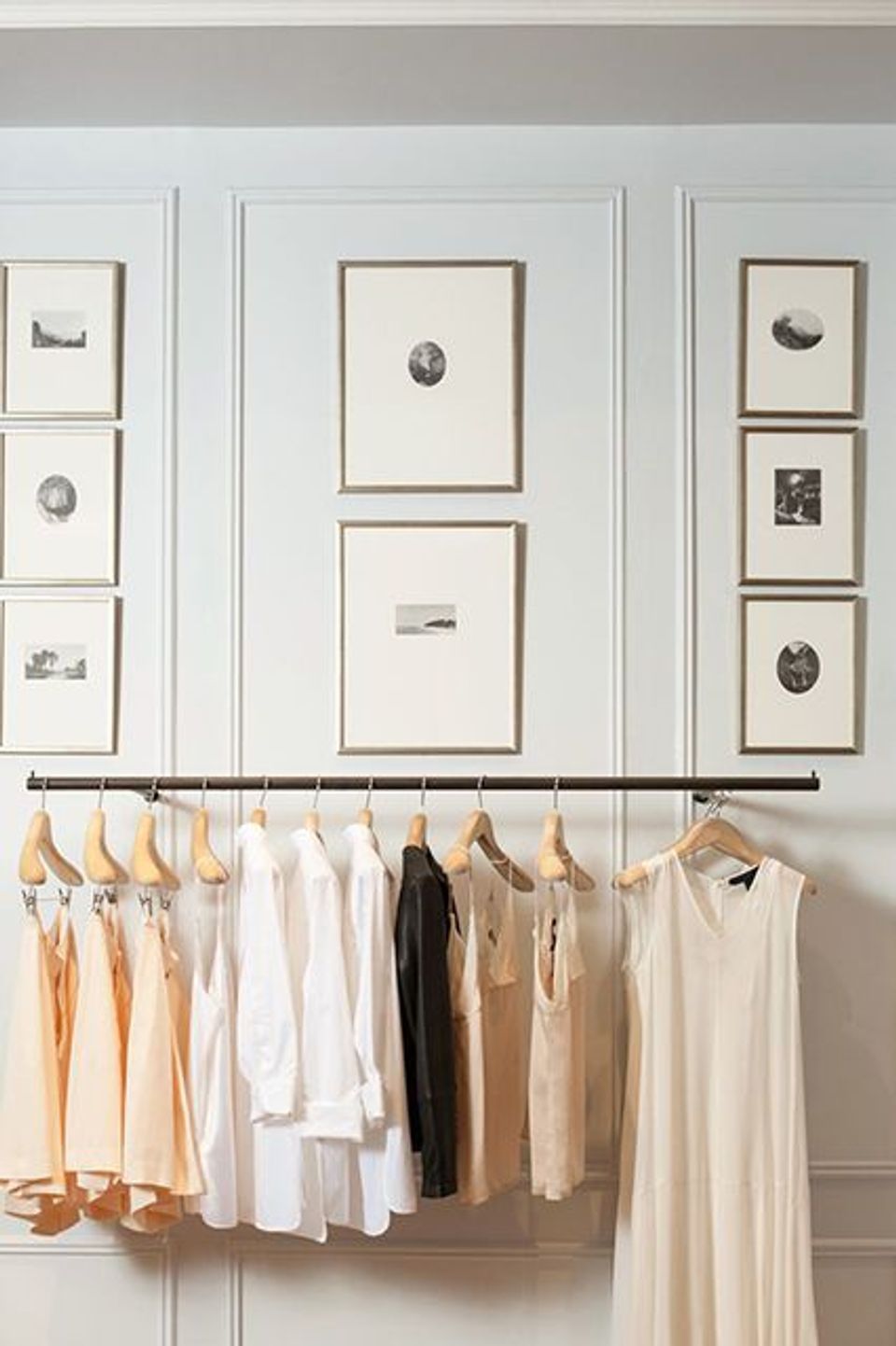 Minimalist closet with symmetrical gallery wall and neutral clothing rack displaying cream, tan, and white pieces
