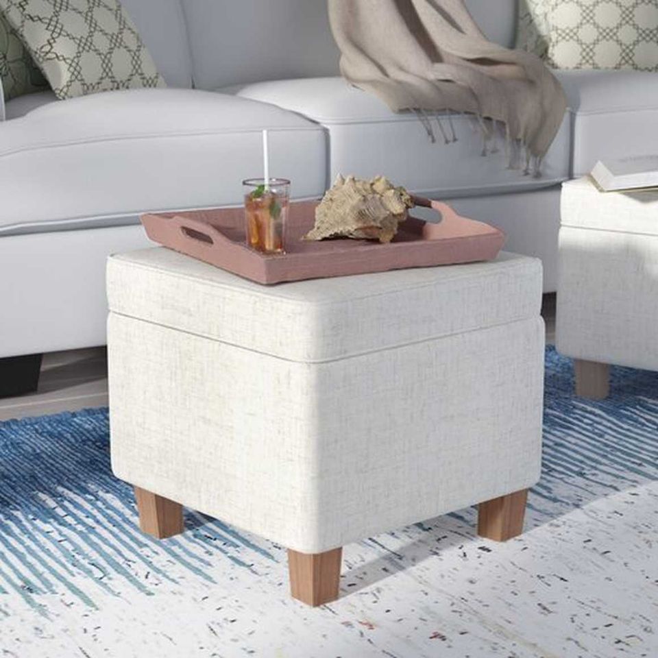 Cream upholstered ottoman with wood legs styled as a functional coffee table with pink tray in bright, airy living room