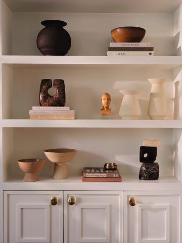 Minimalist white shelving with curated collection of sculptural ceramics and vessels in warm terracotta and deep charcoal tones