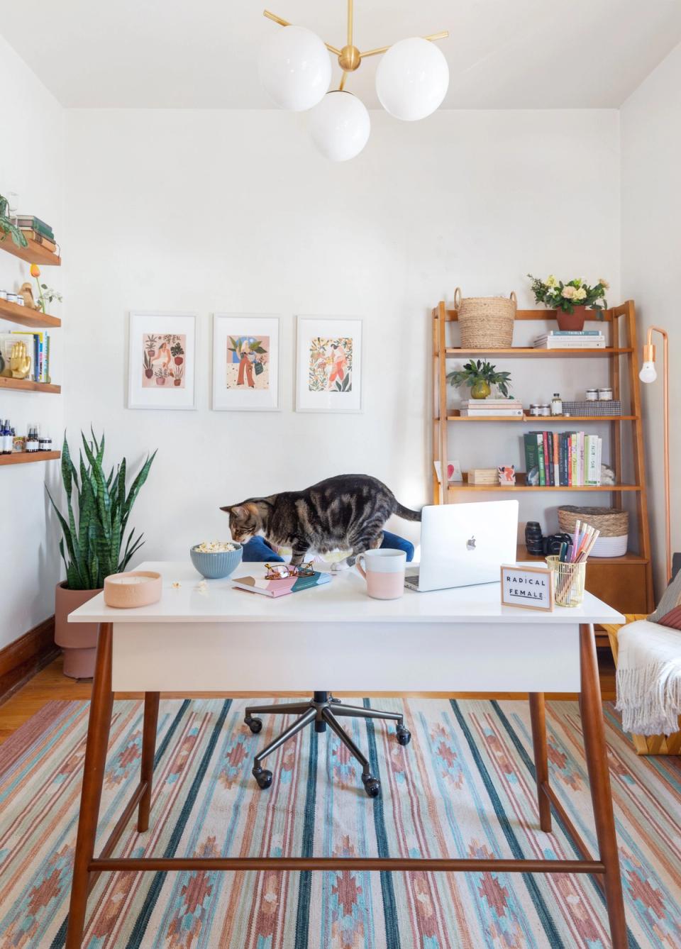 Mid-century modern office with warm wood shelving, gallery wall, and boho striped rug accent