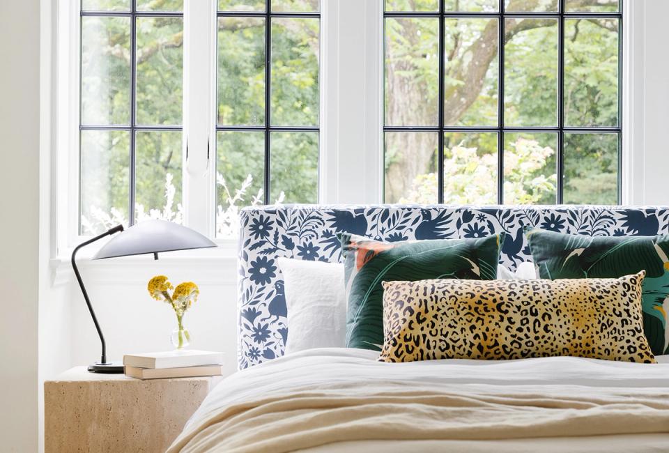 Bright bedroom with blue floral headboard, golden leopard pillow, and forest views from large windows