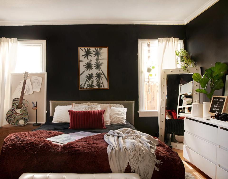 Moody modern bedroom with black walls, burgundy velvet accents, and eclectic styling