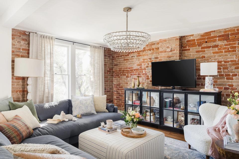 Eclectic living room blending industrial brick, contemporary gray sectional, and warm accents