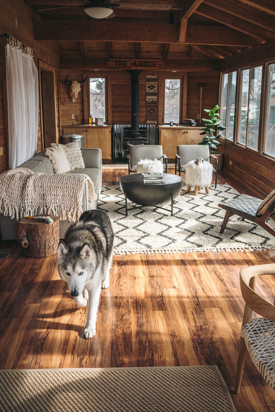 Rustic cabin interior with dark wood beams, geometric rugs, and eclectic furnishings throughout