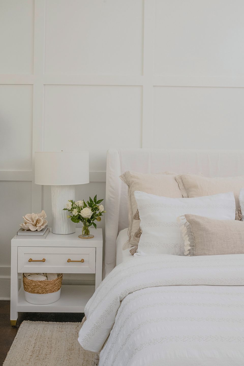 Serene coastal bedroom: white paneled walls, soft neutrals, woven textures, layered pillows
