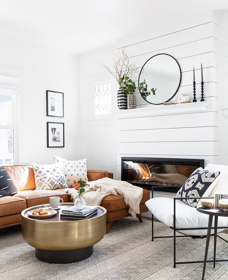 Scandinavian living room with shiplap walls, round black mirror, caramel leather sofa, and warm metallic accents