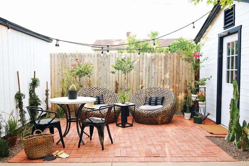 Bohemian garden patio in warm terracotta with woven seating, lush plants, and hanging lights