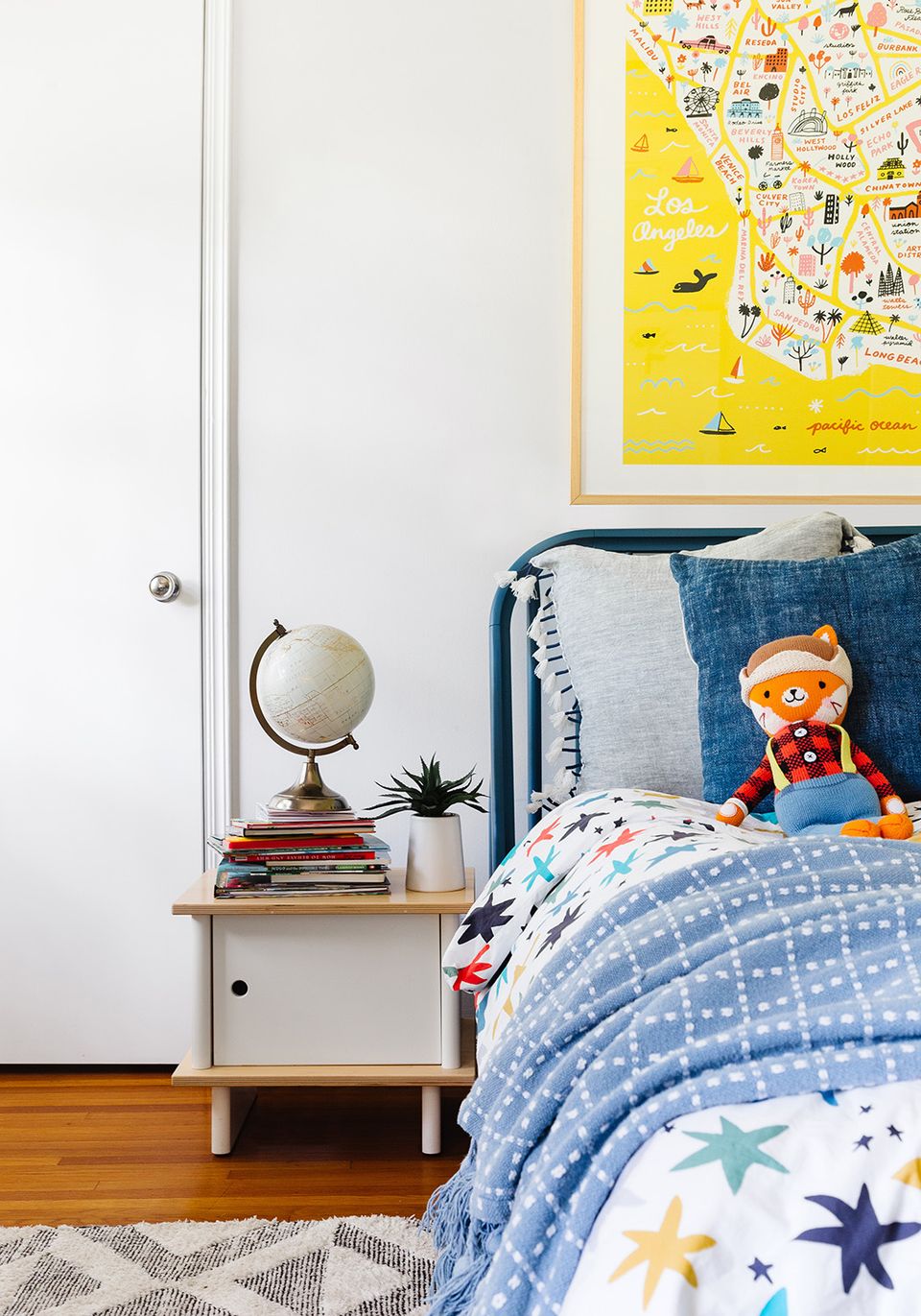 Playful kid's bedroom with yellow map art, blue bedding, and vintage wood nightstand
