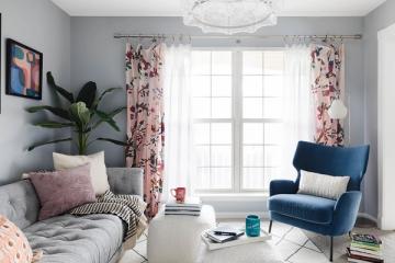Bright bedroom with soft gray walls, floral curtains, navy accent chair, and botanical plants creating a romantic, restful mood