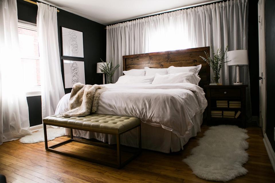 Modern bedroom with black accent wall, rustic wood headboard, neutral bedding, and warm wood flooring