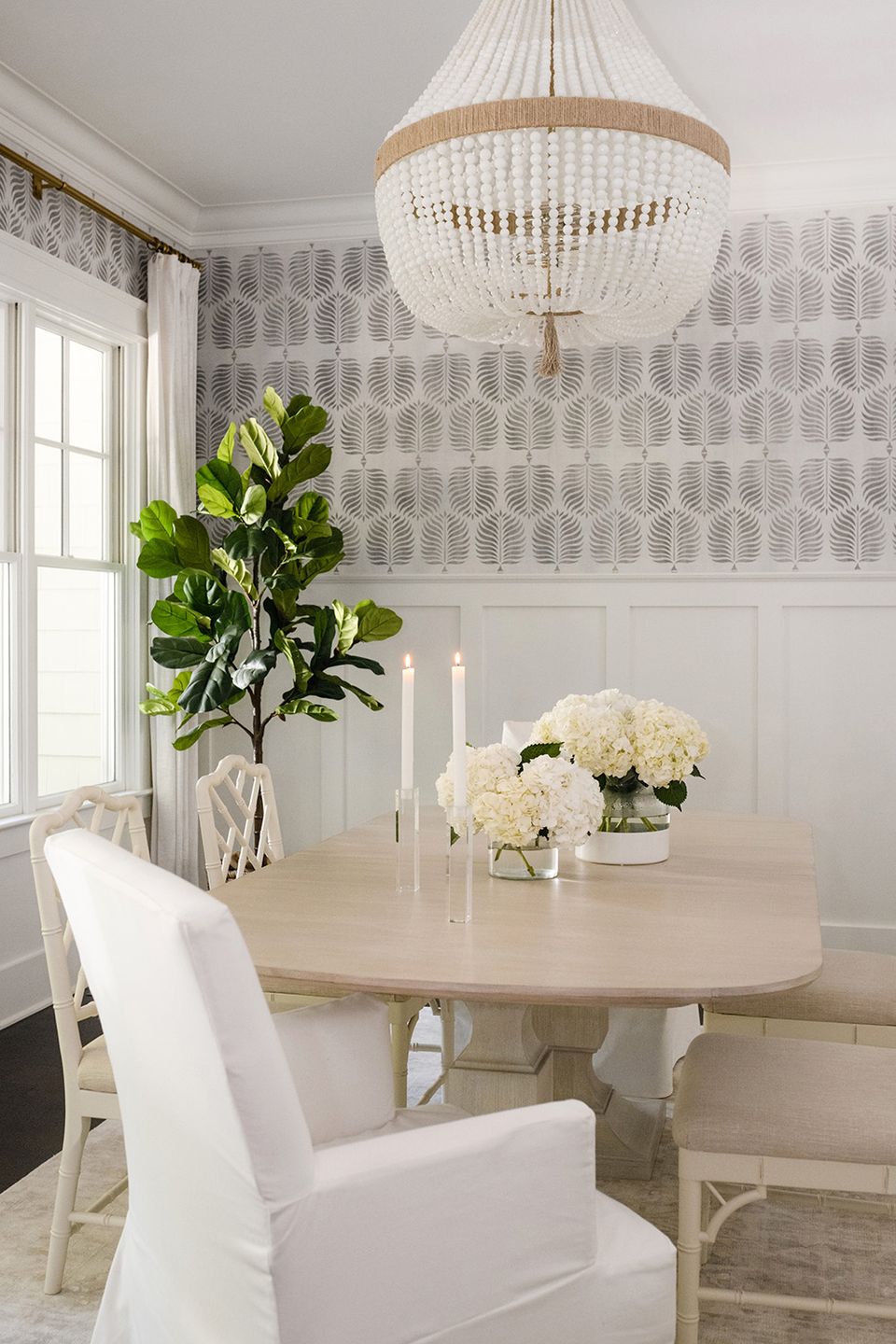 Elegant dining room with patterned wallpaper, picture frame moulding, cream furniture, and beaded chandelier