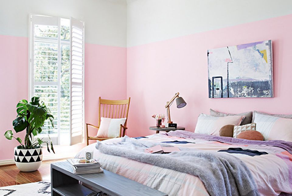 Soft feminine bedroom with blush pink accent wall, pastel bedding, and natural light from shuttered windows.