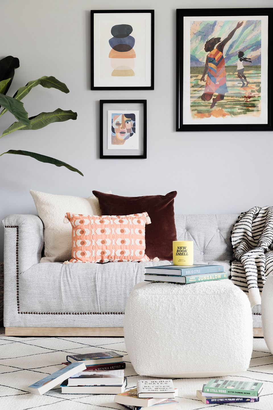Scandinavian reading nook with cream armchair, warm earth-tone pillows, gallery wall art, and cozy ottoman seating.