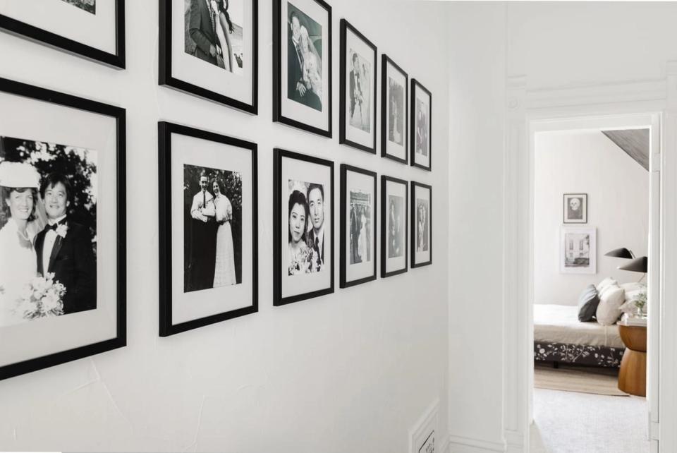 Gallery wall of black-framed black-and-white photographs arranged on clean white walls.