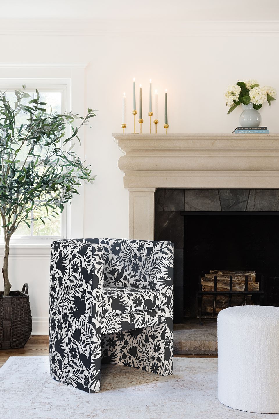 Serene fireplace vignette with botanical black-and-white patterned chair, neutral mantel styling, and fresh greenery accents