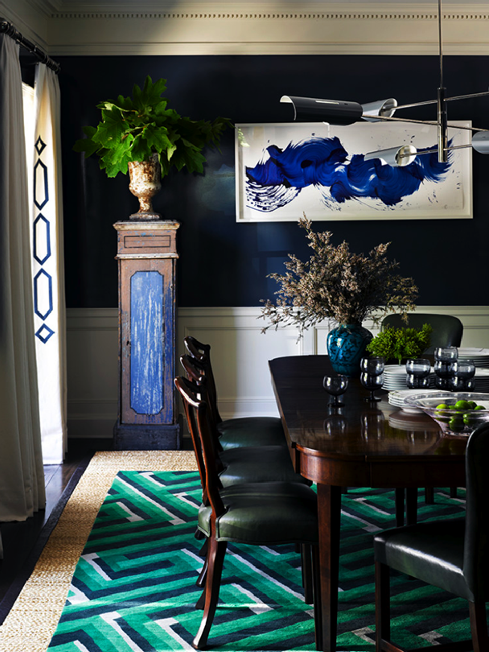 Contemporary dining room with dramatic navy walls, emerald geometric rug, and bold blue abstract artwork
