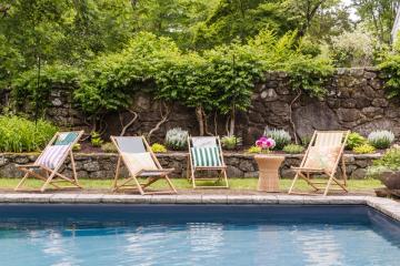 Classic poolside retreat with striped lounge chairs, manicured hedges, and timeless nautical elegance by sparkling blue water.