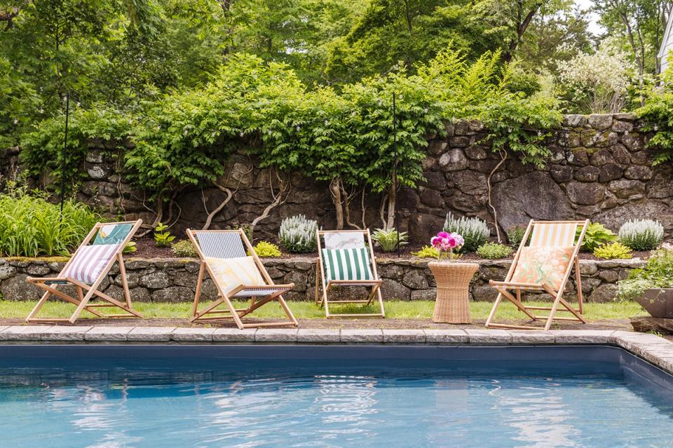 Poolside retreat with classic canvas deck chairs and lush green landscaping suggesting understated luxury