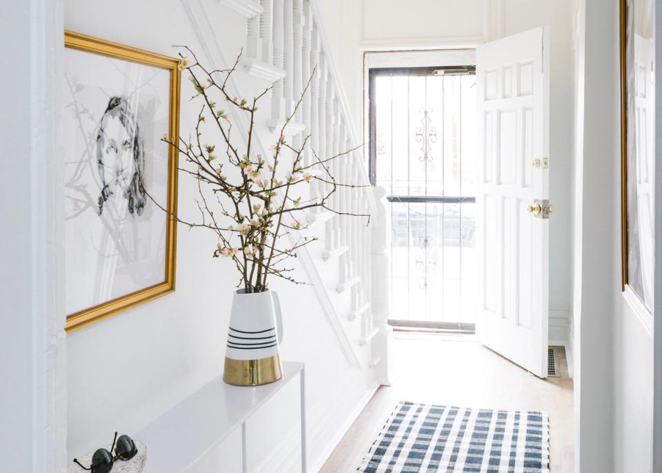 Minimalist entryway with white walls, brass-framed art, dried branches in striped vase, and black-and-white geometric runner rug