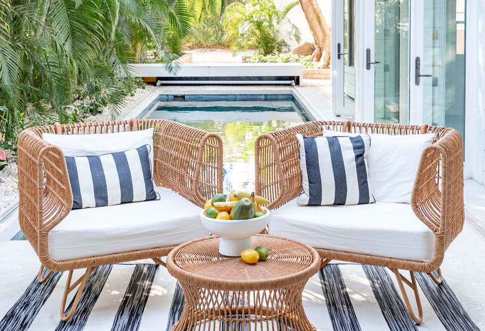 Coastal poolside seating with woven rattan chairs, navy striped pillows, and natural materials creating a breezy, nautical retreat.