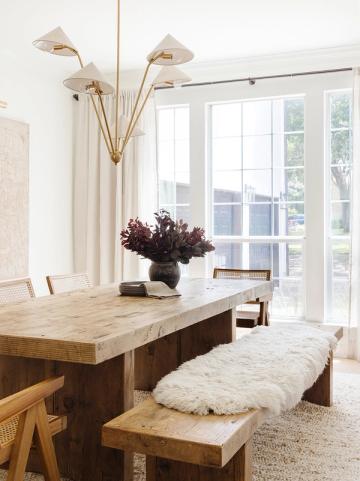 Minimalist dining space with sculptural brass chandelier, dark burgundy florals, and light wood furniture