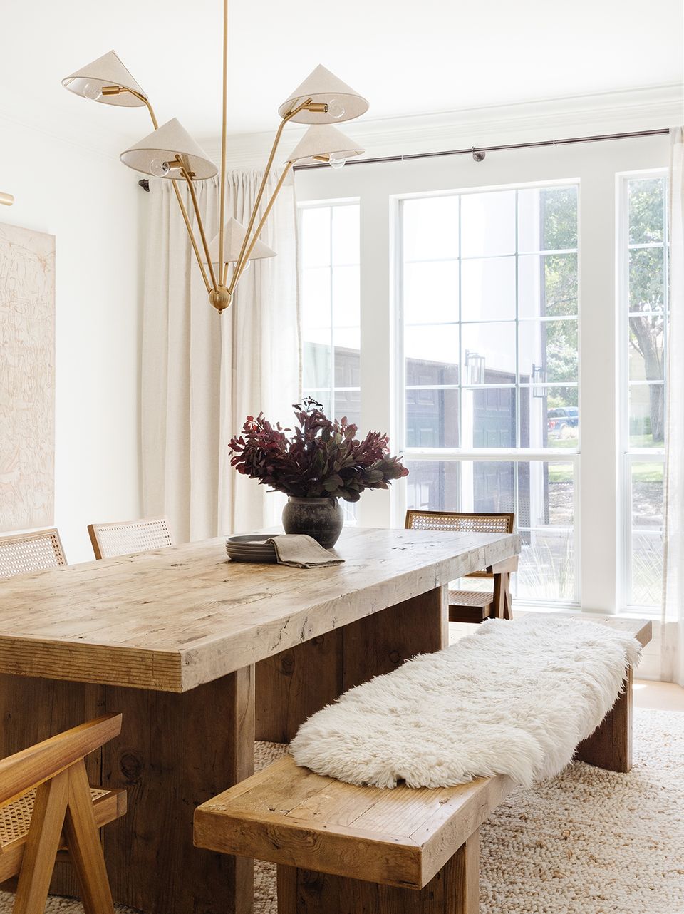 Minimalist dining space with sculptural brass chandelier, dark burgundy florals, and light wood furniture