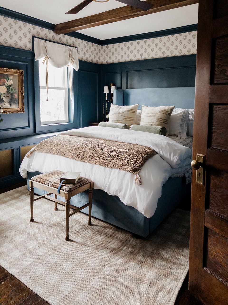 Dark teal canopy bed with layered patterns, neutral bedding, and wood ceiling beams