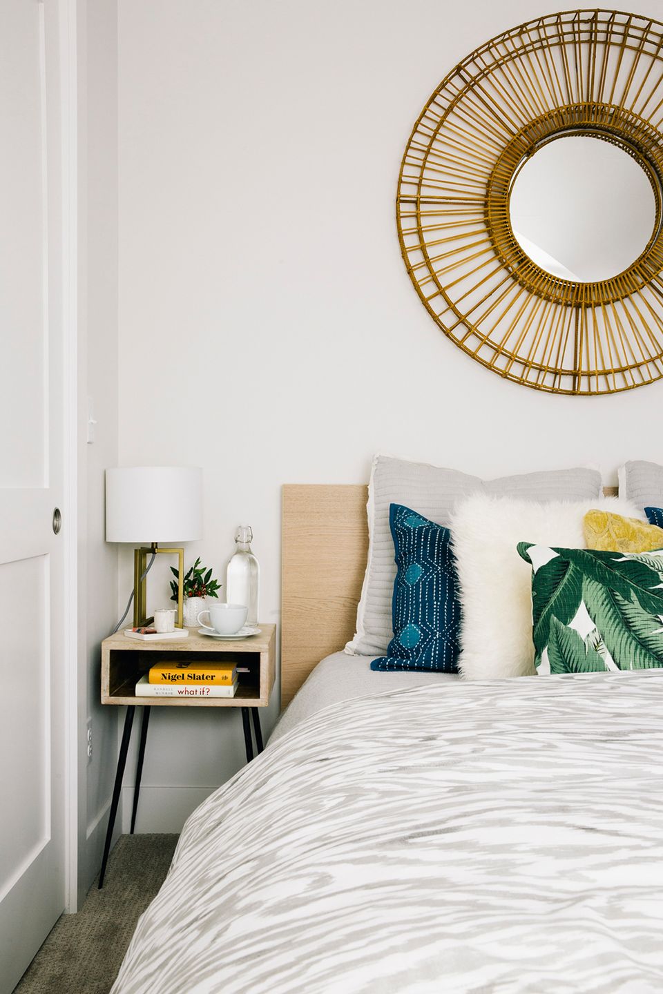 Modern boho with rattan wall mirror, natural headboard, emerald accents, and minimalist styling