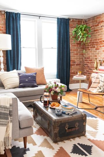 Industrial-chic loft with exposed brick, navy curtains, and vintage steamer trunk coffee table