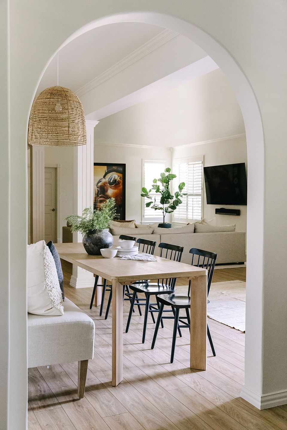 Bright Scandinavian dining area with arched doorway, natural wood table, and potted greenery