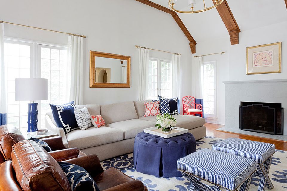 Bright living room with navy and coral accents, wooden beams, and gold-framed mirror above gray sofa