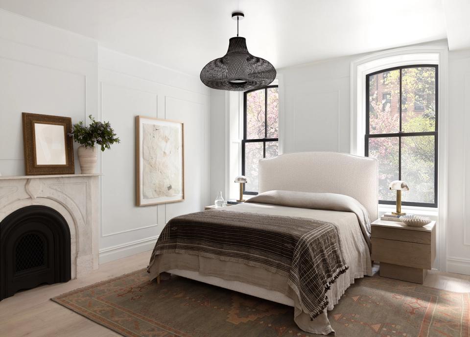 Bright farmhouse bedroom with fireplace, white shiplap walls, black pendant light, and warm wood tones evoking cozy elegance