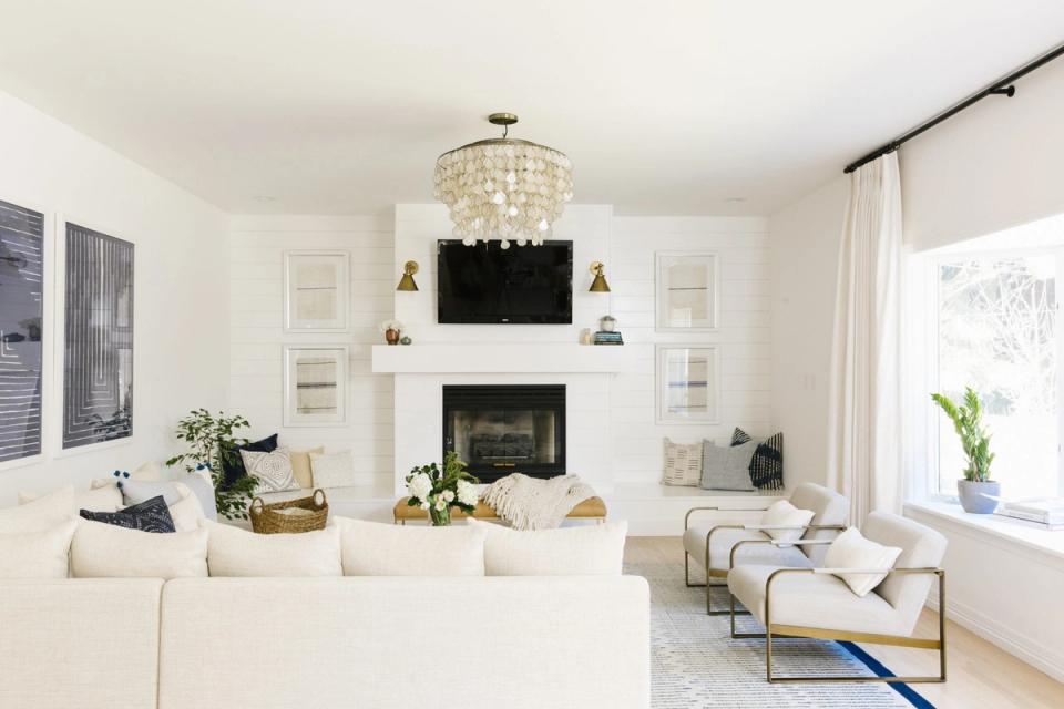 Bright, symmetrical living room with cream palette, fireplace focal point, crystal chandelier, and geometric accent chair