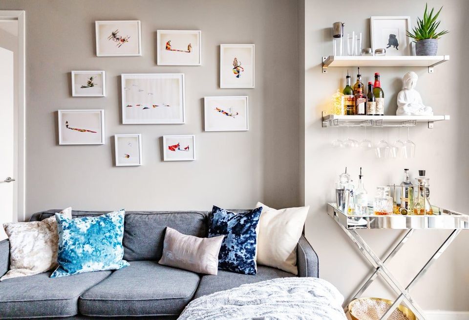 Modern living room with gray sofa, blue patterned pillows, gallery wall art, and styled bar cart shelving with ambient lighting