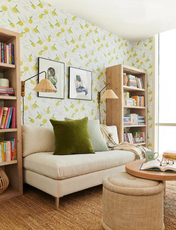 Playful reading nook with yellow leaf wallpaper, floating frames, built-in wood shelving, cream chair, and bohemian warmth.