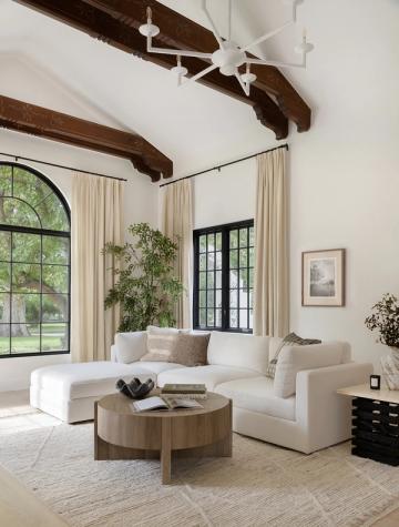 Serene organic modern lounge with dark exposed beams, cream seating, natural wood coffee table, and abundant greenery