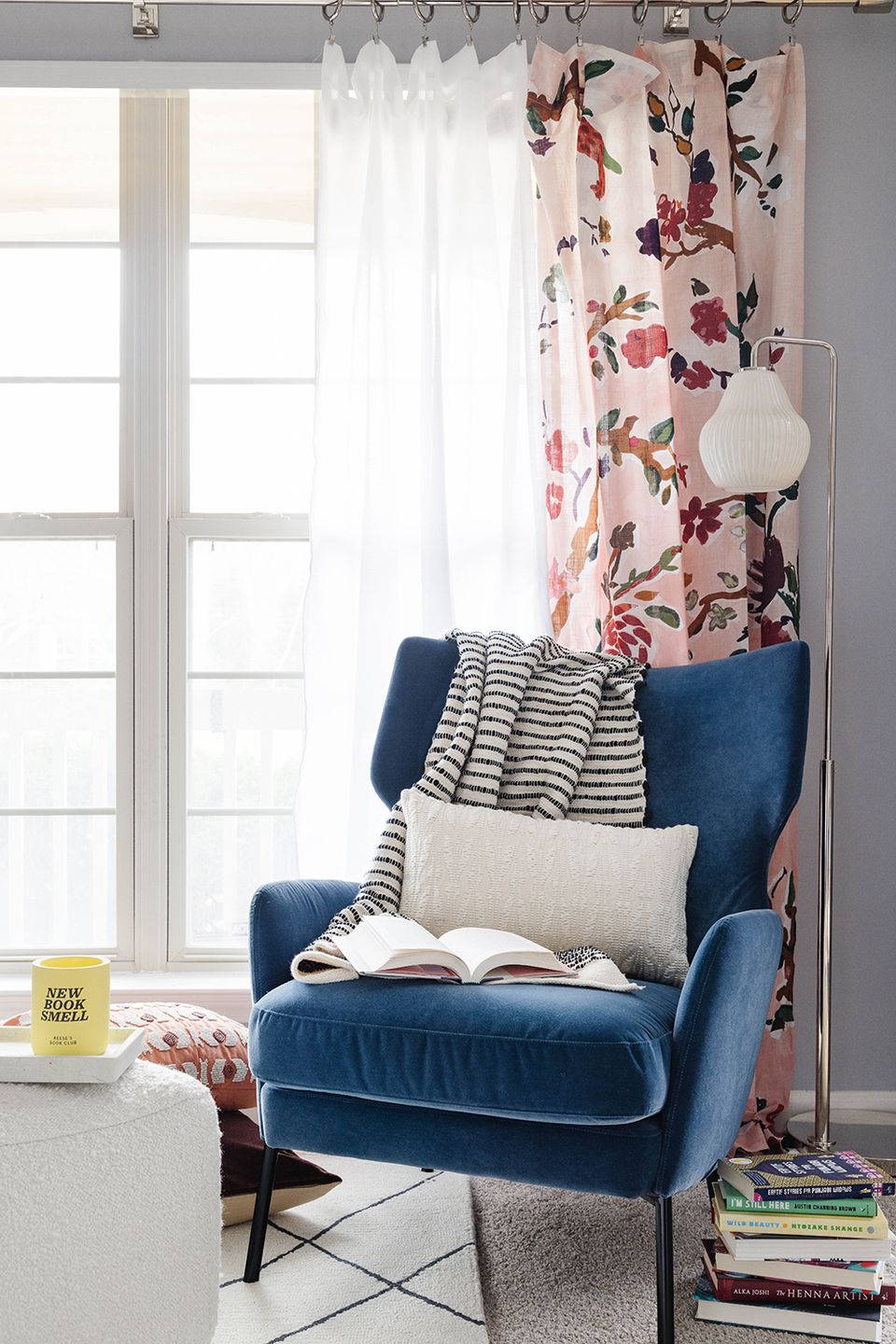 Cozy window seat with navy velvet chair, floral curtains, striped throw, and layered textiles in pink and blue tones
