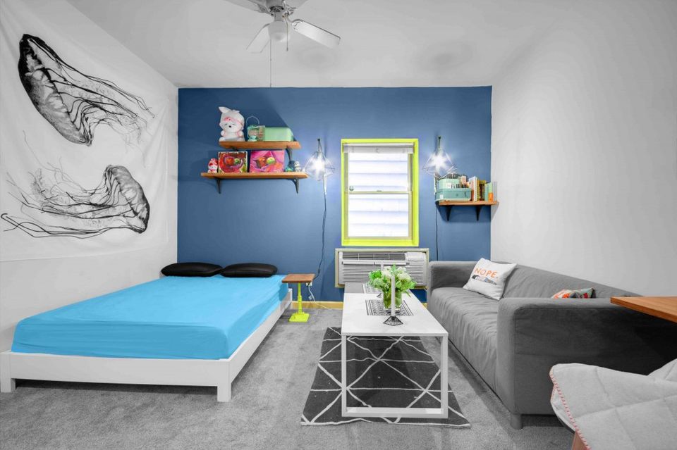 Bright studio blending navy accent wall, turquoise bed, gray sofa, and modern geometric side table