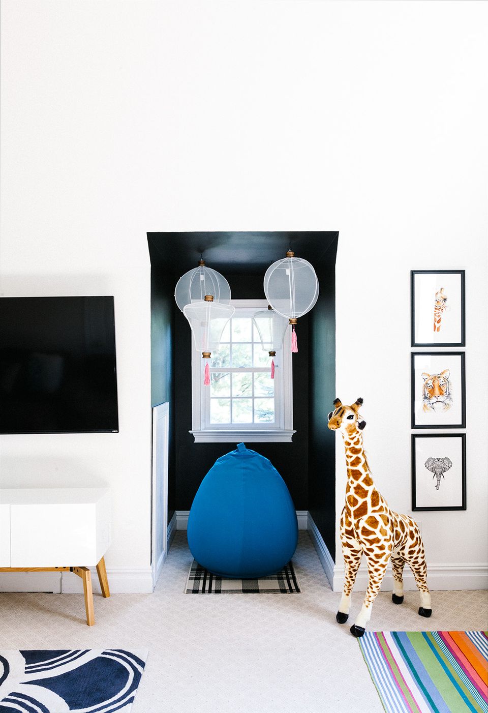 Contemporary playroom with bold black reading alcove, bright blue chair, and minimalist gallery wall