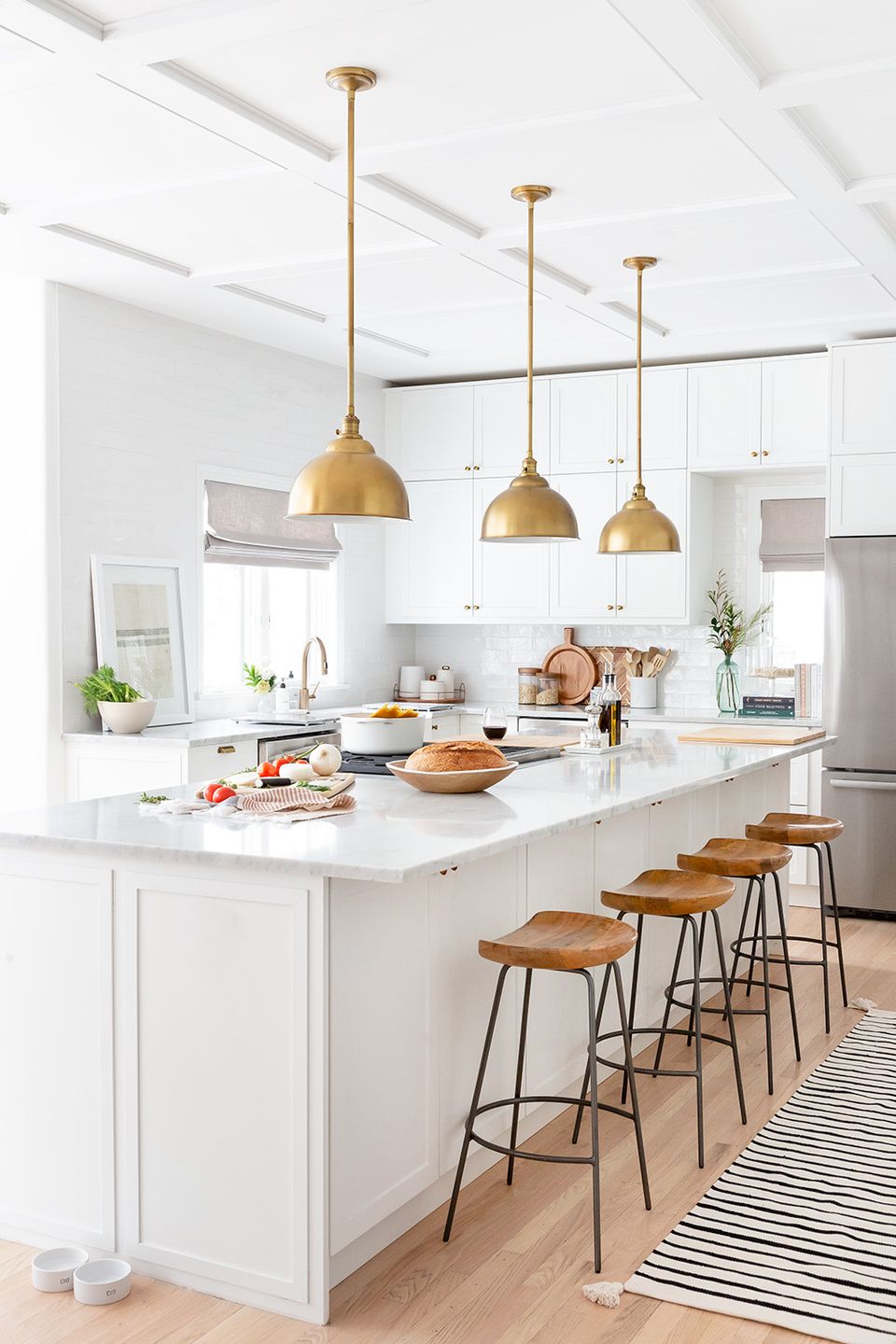 Bright transitional kitchen with white cabinetry, brass pendant lights, and natural wood bar seating